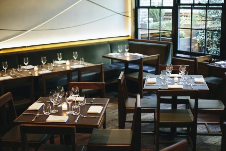 Interior view of a restaurant featuring wooden tables set with glassware and cutlery.
